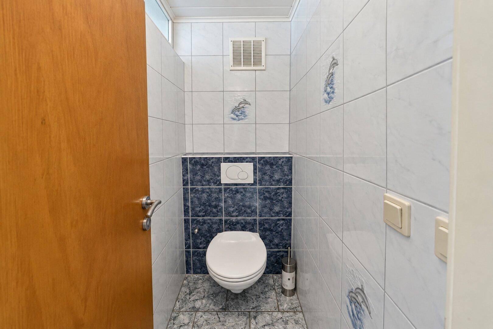 Kleines WC mit wandhängender Toilette, blau-weißen Fliesen und Lüftung.