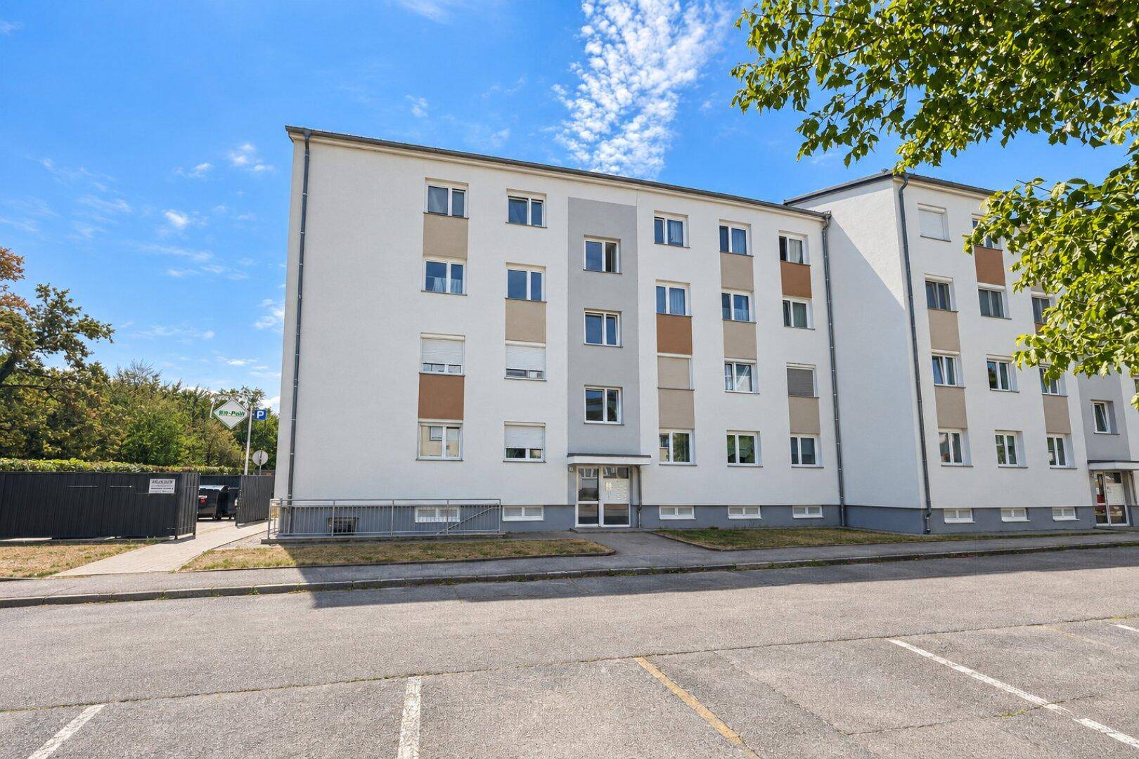 Mehrstöckiges Wohngebäude mit moderner Fassade, Parkplätzen und grüner Umgebung.