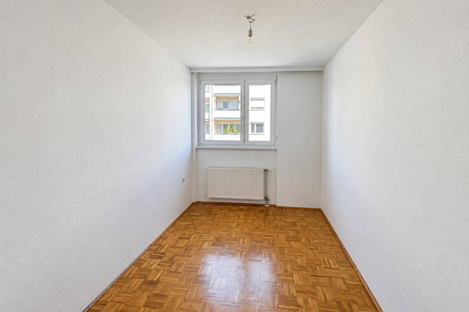 Helles Schlafzimmer mit Parkettboden, weißen Wänden und Blick auf die Nachbarschaft.