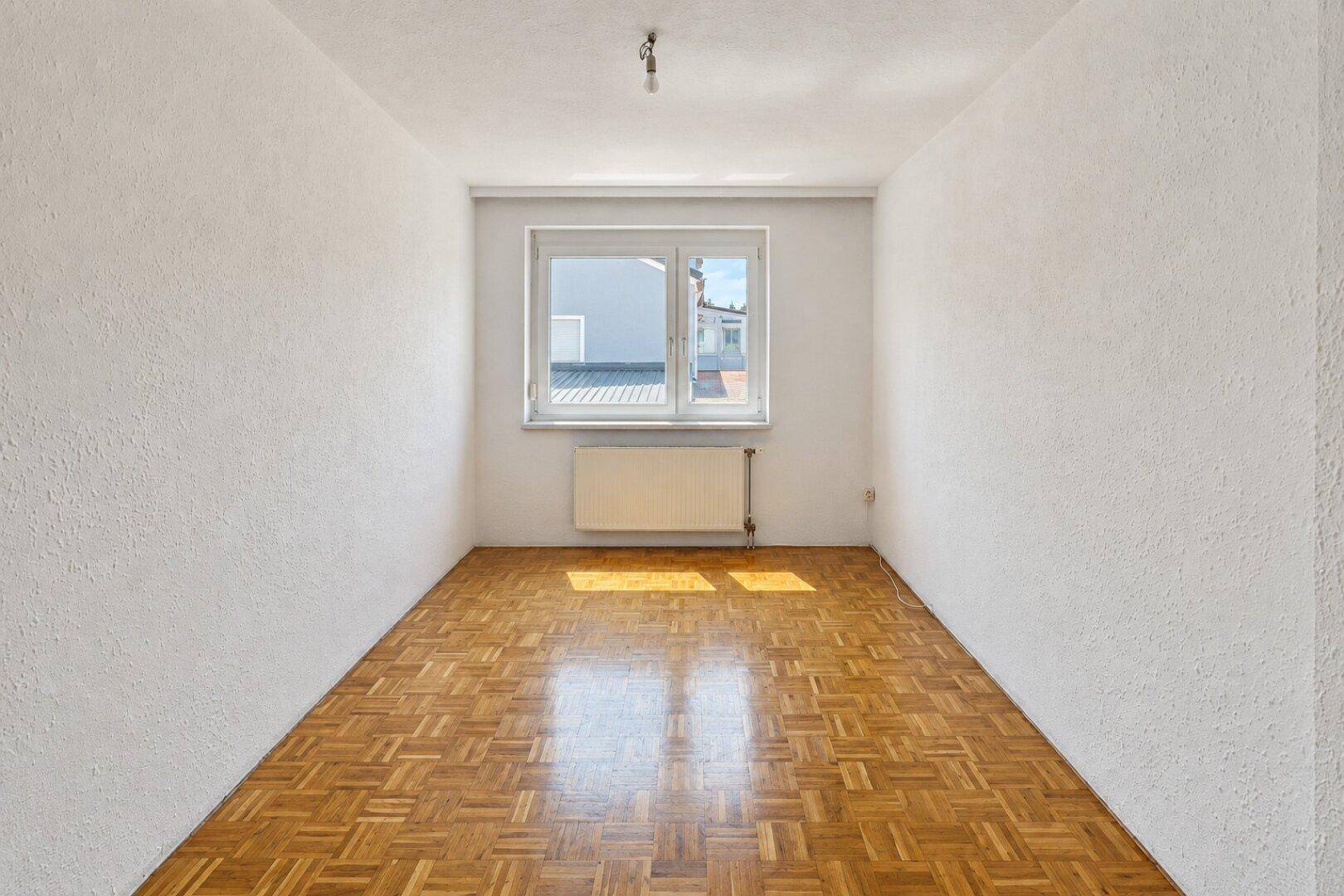 Helles Zimmer mit Parkettboden, weißen Wänden und viel natürlichem Sonnenlicht.