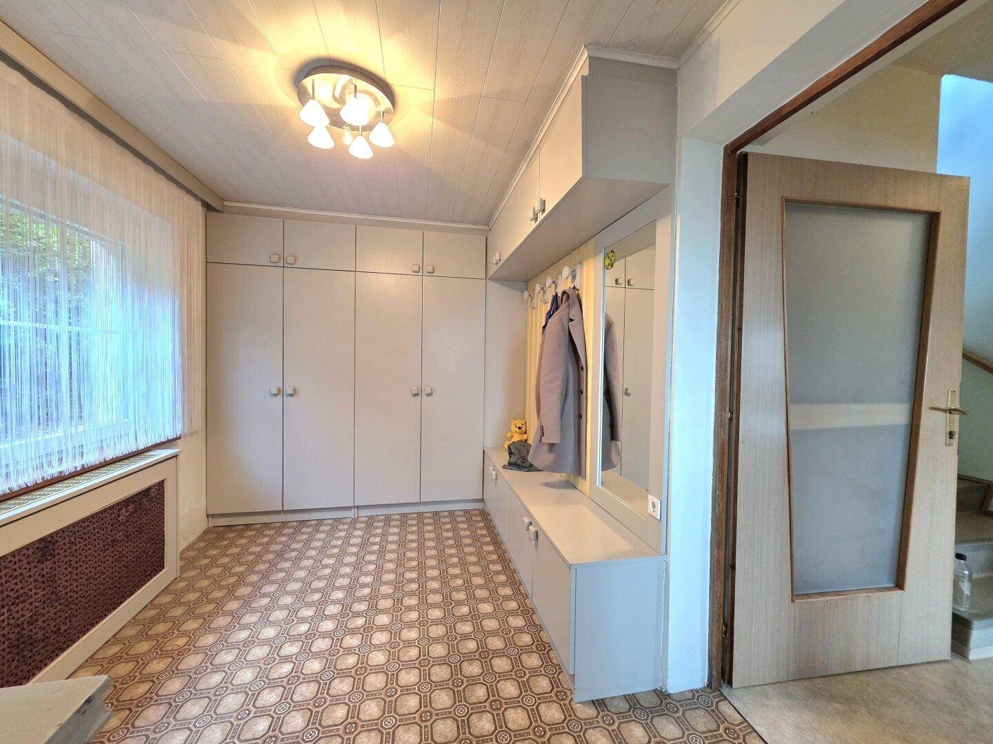 Heller Flur mit Einbauschränken, Garderobe und einem Fenster, das Tageslicht hereinlässt.