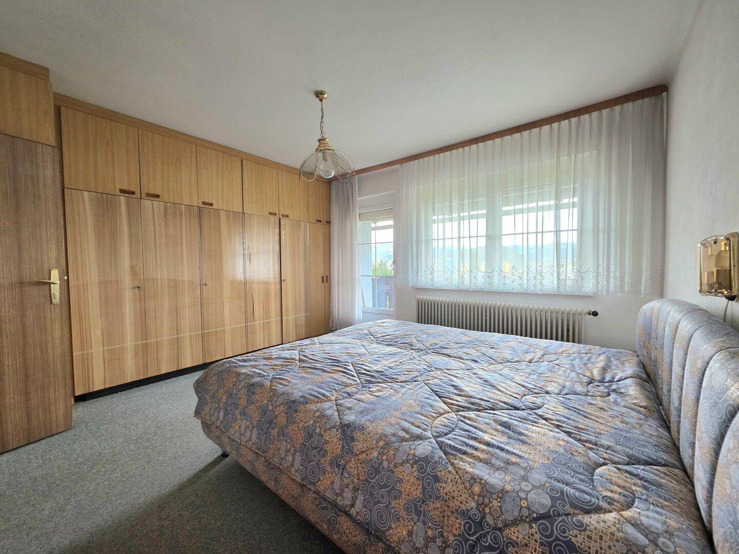 Schlafzimmer mit großem Bett, Holzschränken und einem Fenster mit Blick auf die Umgebung.