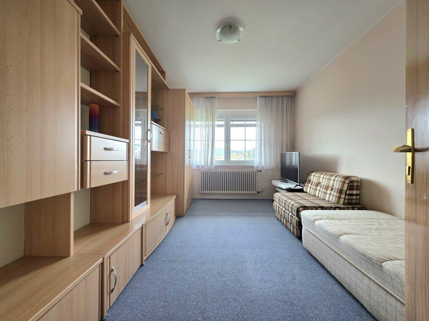 Helles Schlafzimmer mit Teppichboden, Holzregalen und einem Einzelbett, gut beleuchtet.