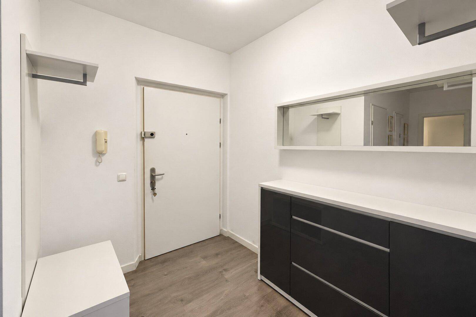 Eingangsbereich mit dunklem Sideboard, Spiegel und Laminatboden.