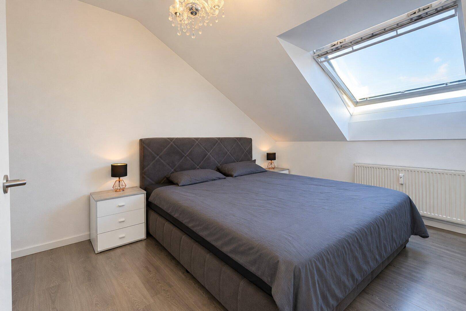 Gemütliches Schlafzimmer mit Doppelbett, Dachschräge und großem Dachfenster.