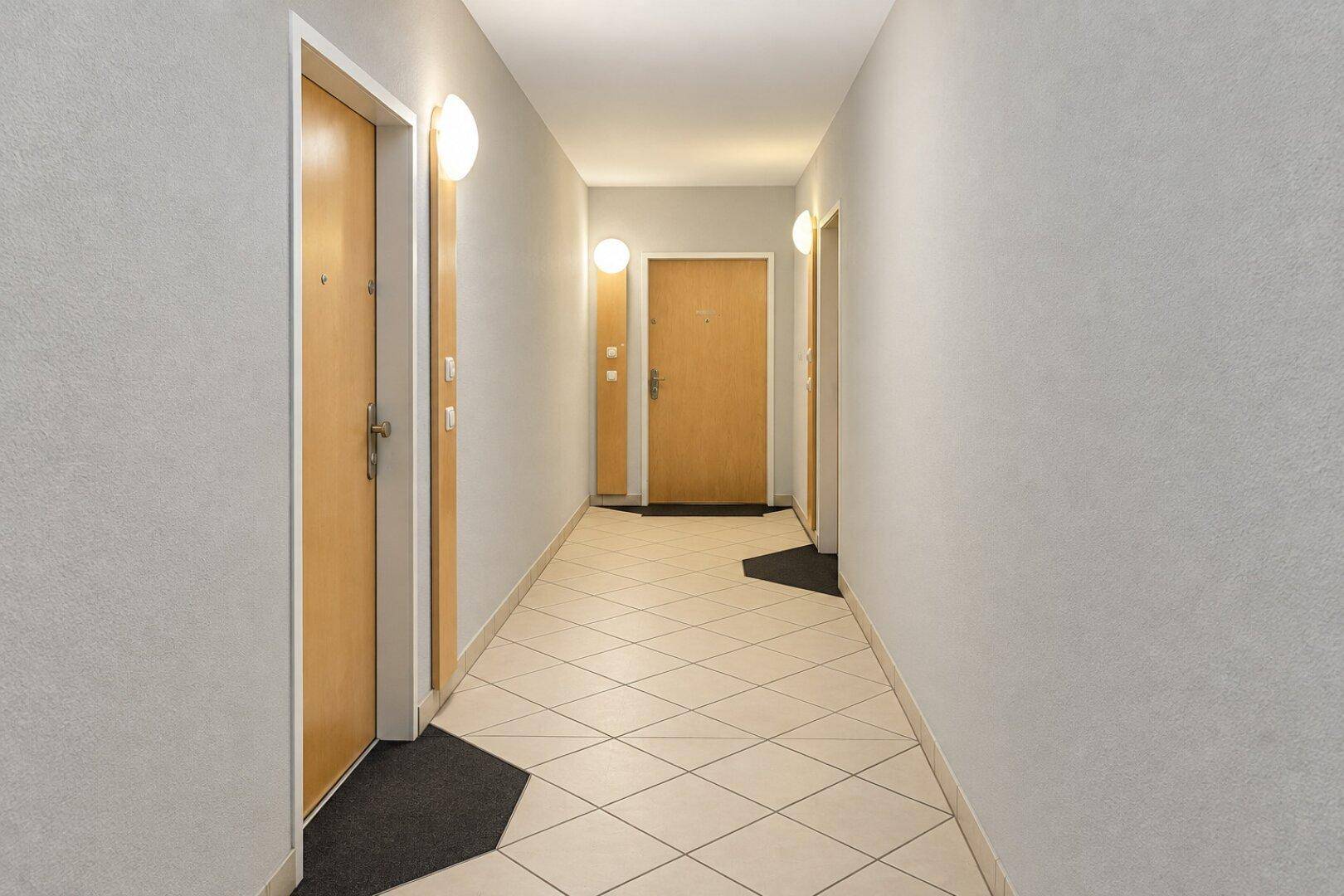 Heller Gemeinschaftsflur mit Fliesenboden und mehreren Wohnungstüren.