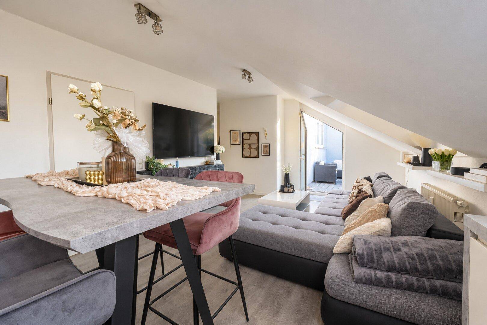 Offener Wohn- und Essbereich mit großem Sofa, Esstisch und Zugang zum Balkon.