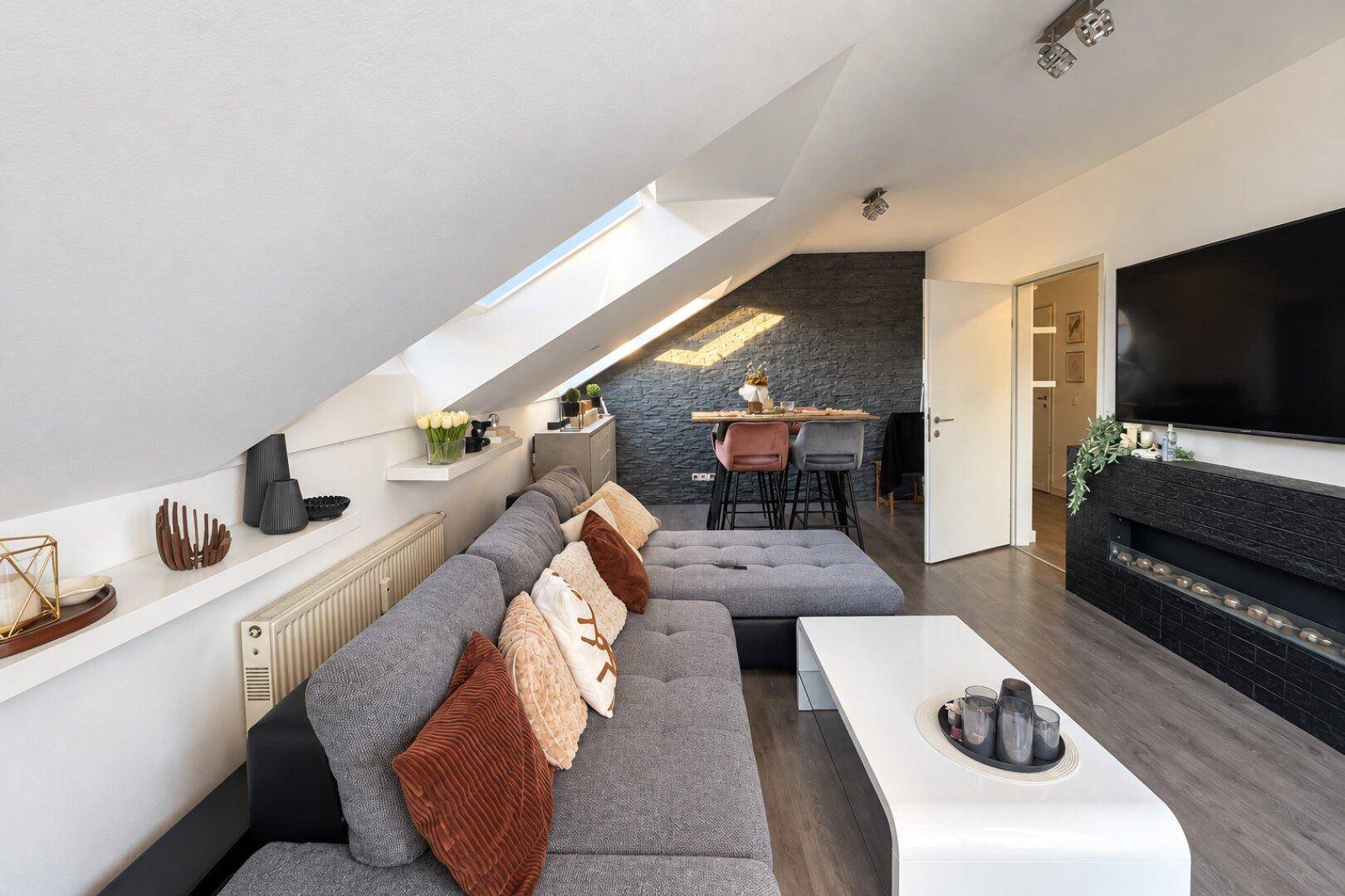 Geräumiges Wohnzimmer mit großem Sofa, Dachschräge und Blick auf den Essbereich.