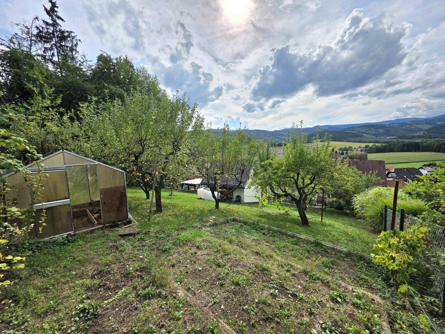 Großer Garten mit Obstbäumen, Gewächshaus und weitem Blick auf die umliegende Natur.