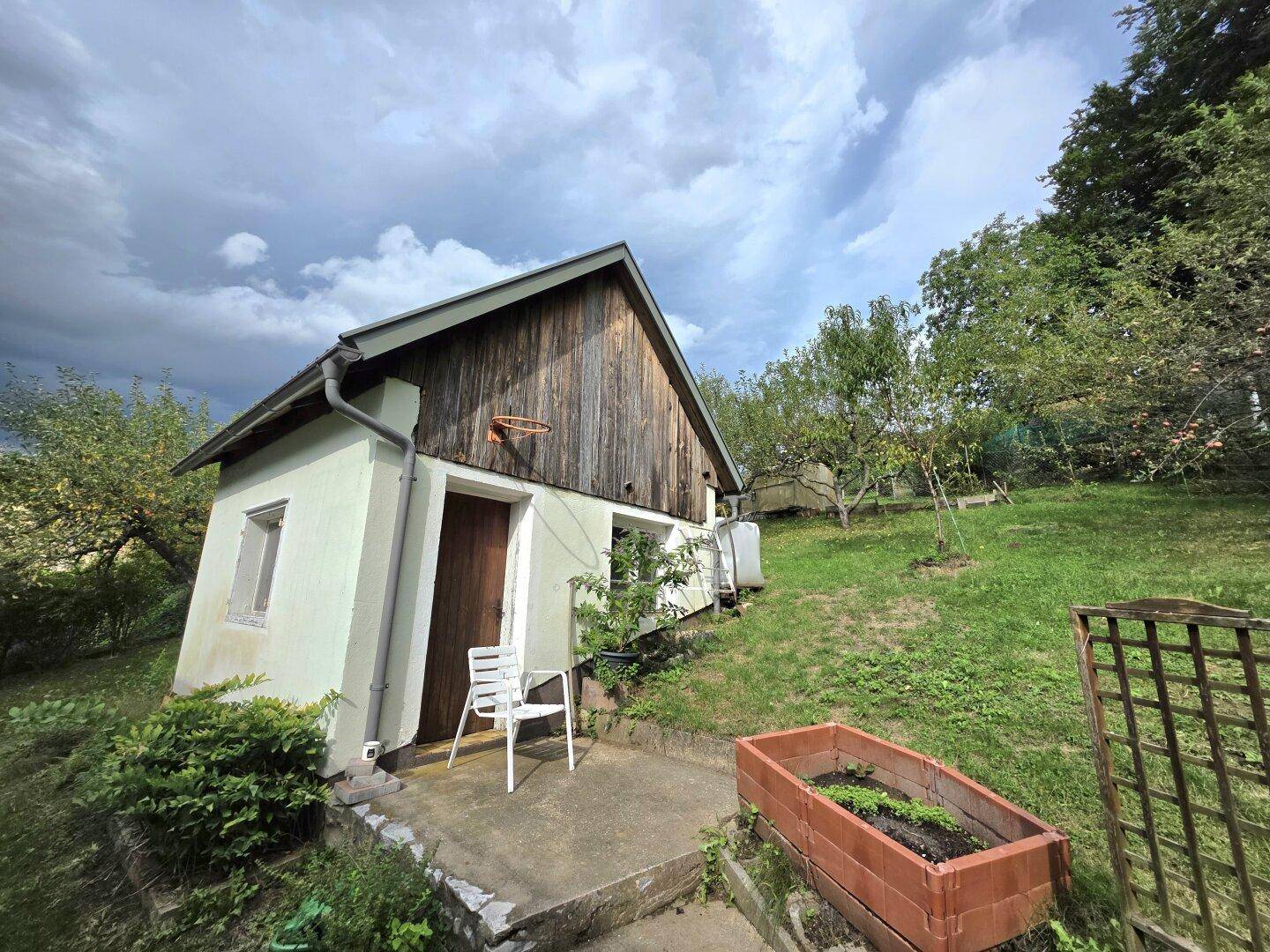 Kleines Nebengebäude im Garten mit Holzfassade und Blick auf die grüne Umgebung.