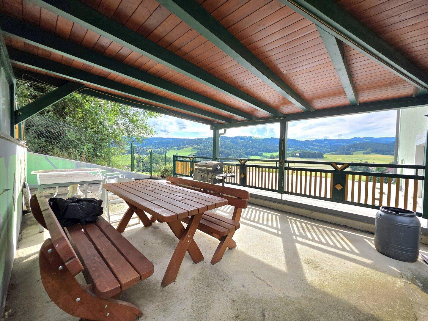 Überdachte Terrasse mit Holztisch und Bänken, ideal für Mahlzeiten im Freien mit schöner Aussicht.