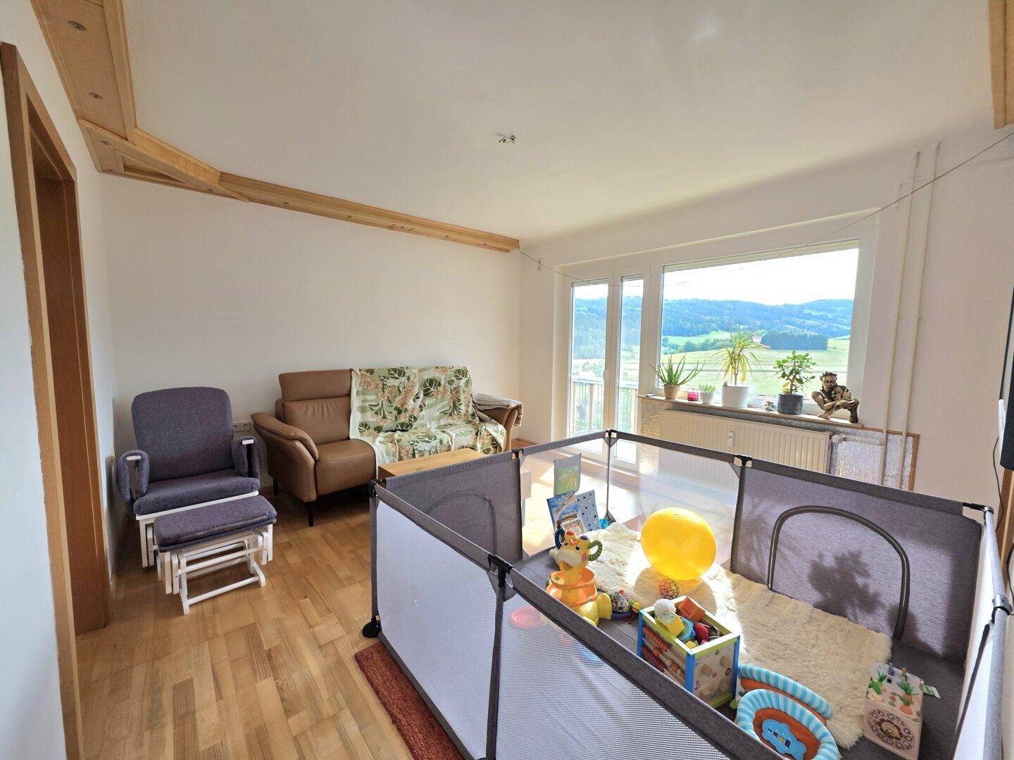 Helles Wohnzimmer mit Holzboden, gemütlichen Sofas und großem Fenster mit Landschaftsblick.