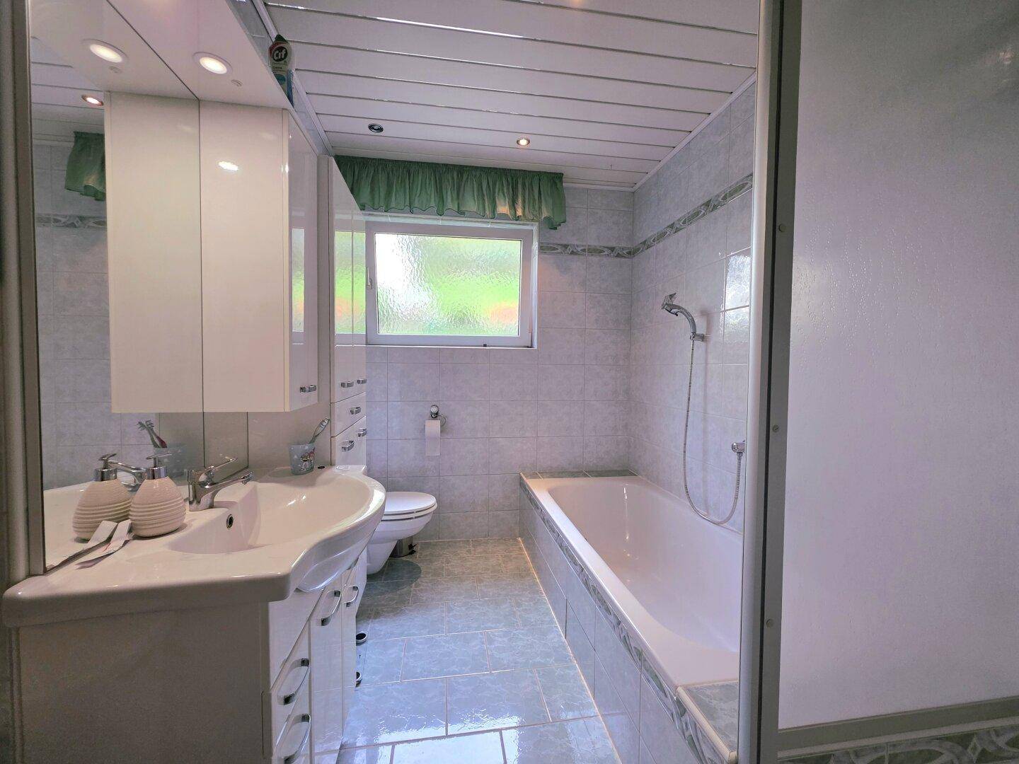 Badezimmer mit Badewanne, Waschbecken, Spiegelschrank und hellen Fliesen.