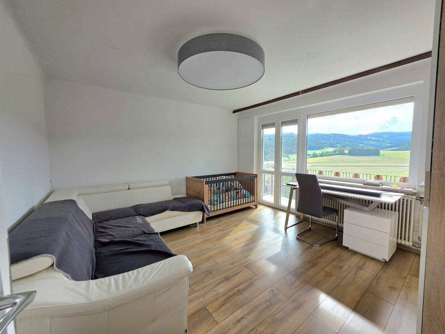 Heller Wohnbereich mit Sofa, Schreibtisch und großem Fenster mit weitem Landschaftsblick.