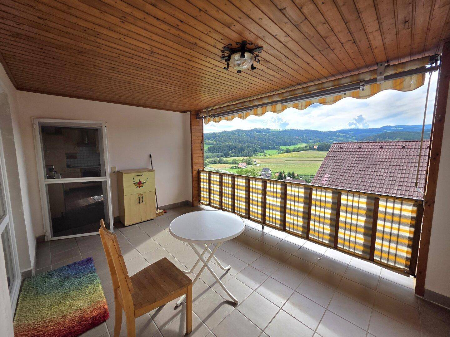 Überdachter Balkon mit Markise, Tisch und Stühlen, bietet einen weiten Blick über die Landschaft.