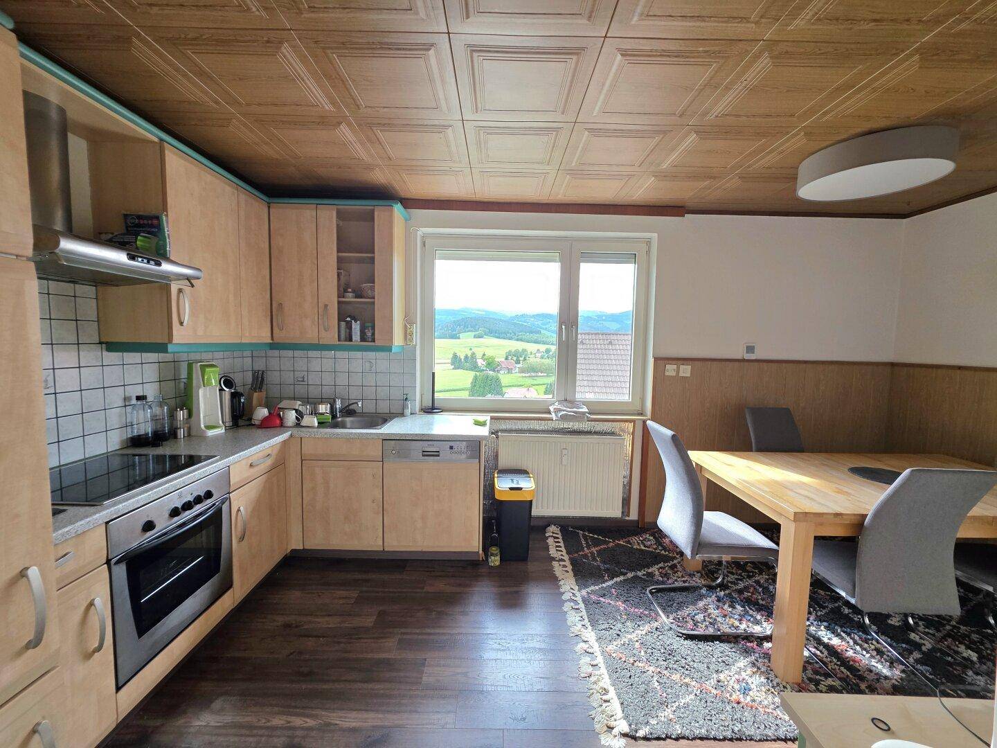 Geräumige Küche mit Essbereich, Holzschränken und Fenster mit Blick auf die grüne Umgebung.