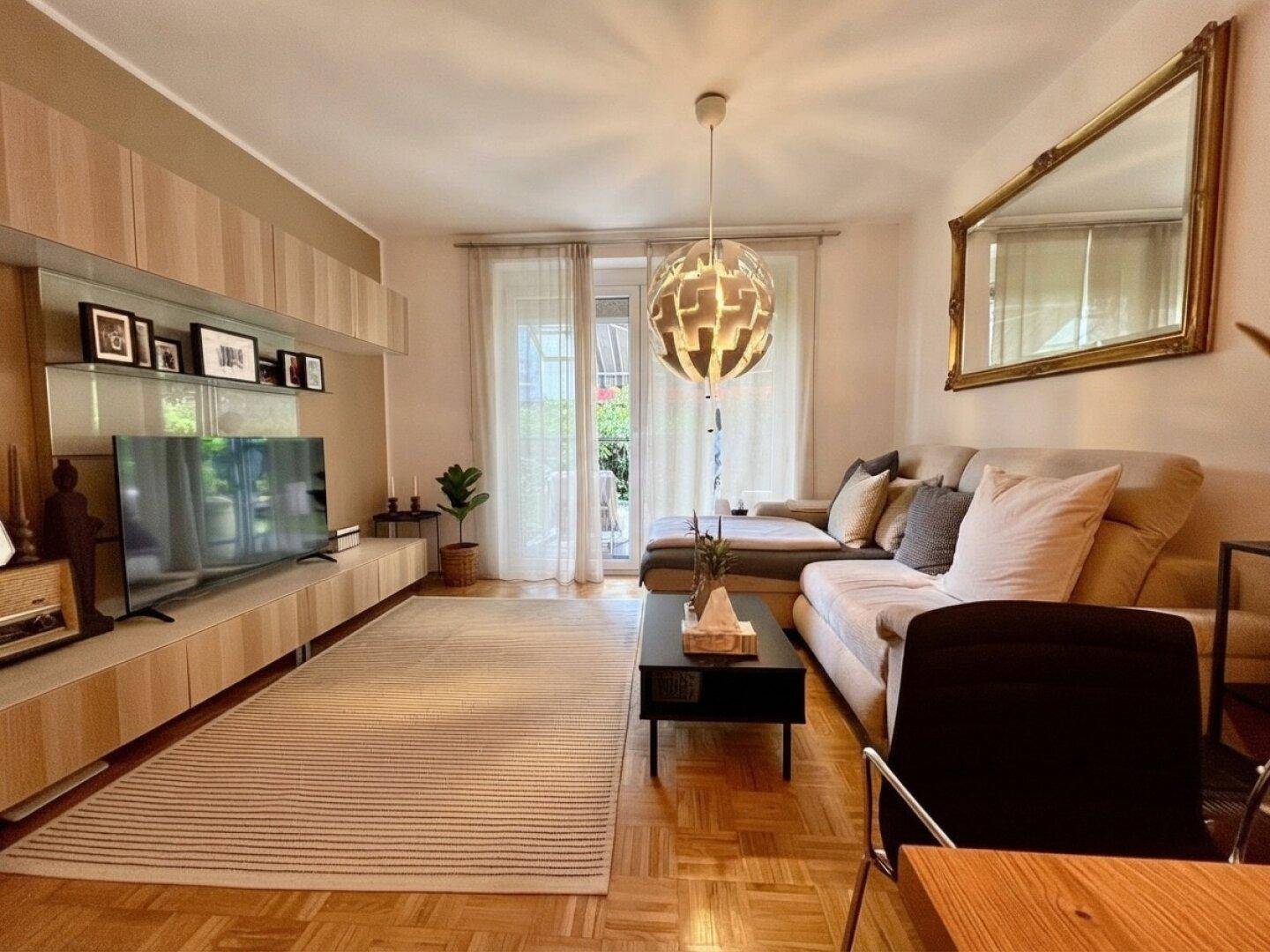 Helles Wohnzimmer mit Parkettboden, moderner Einrichtung und Zugang zu einem Außenbereich.