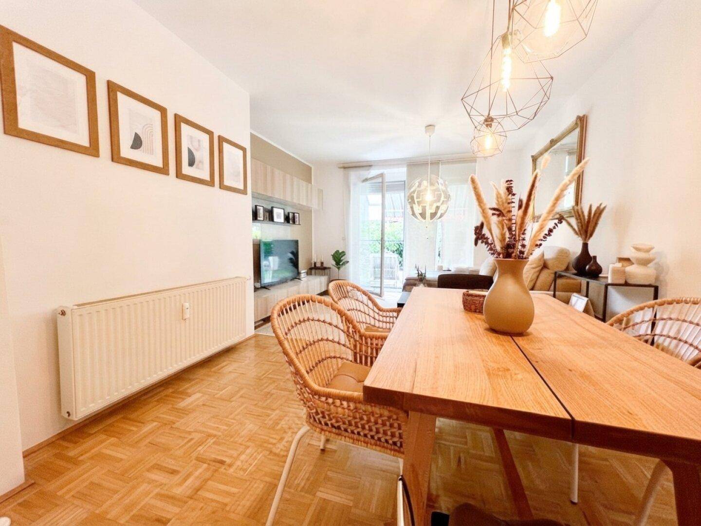 Offener Wohn- und Essbereich mit Holztisch, Rattan-Stühlen und Parkettboden.
