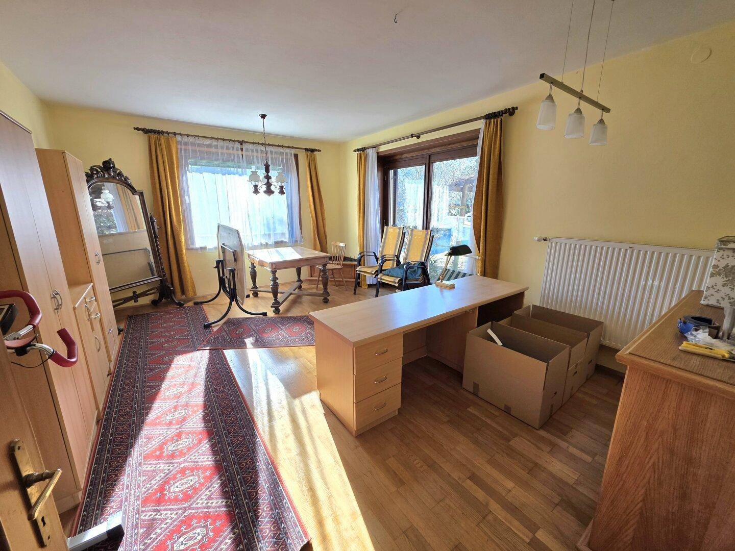 Geräumiges Arbeitszimmer mit Holzschreibtisch, Teppich und großen Fenstern, die den Raum erhellen.
