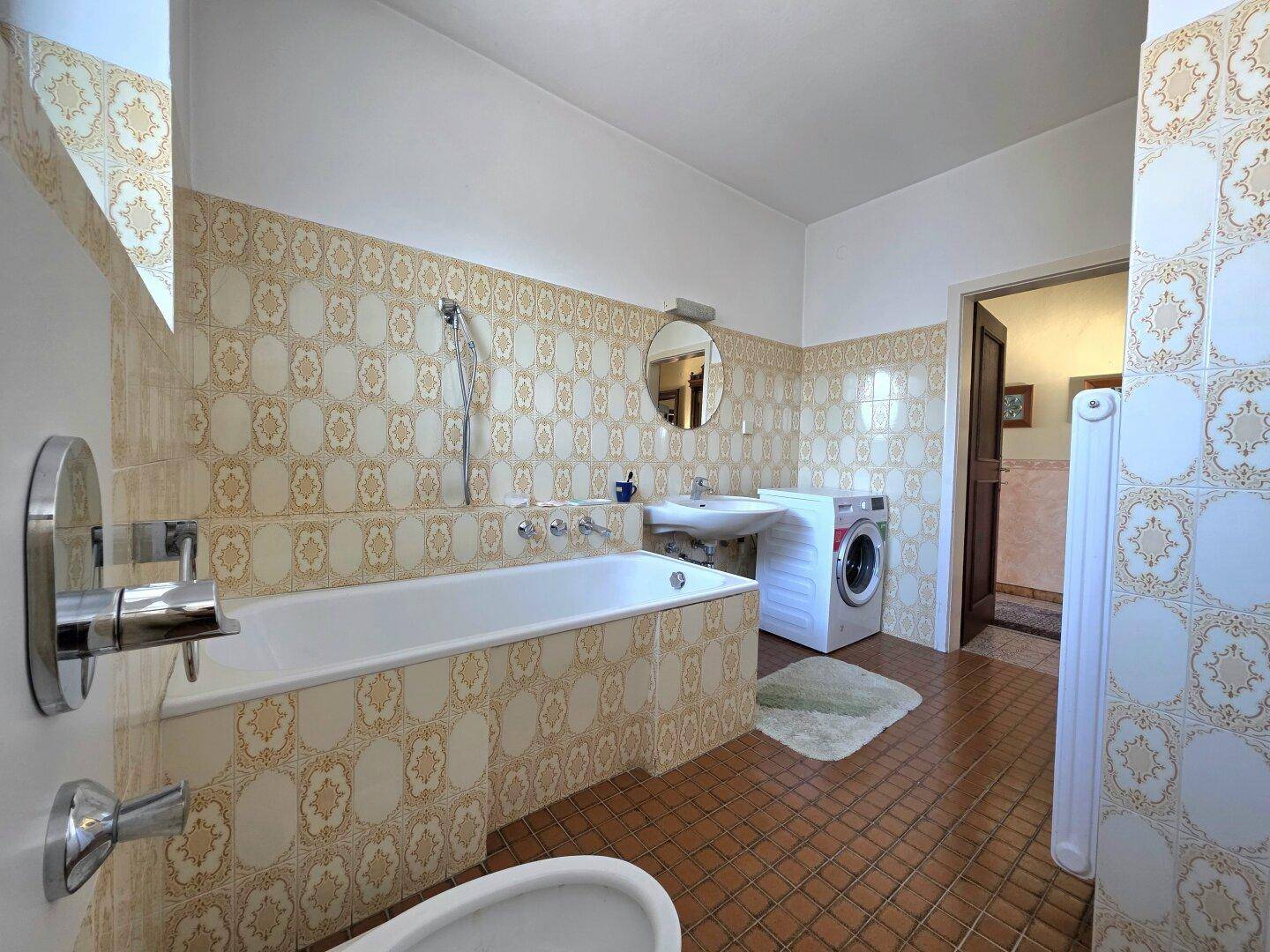 Badezimmer mit Badewanne, Waschbecken und Waschmaschine, dekoriert mit gemusterten Fliesen.
