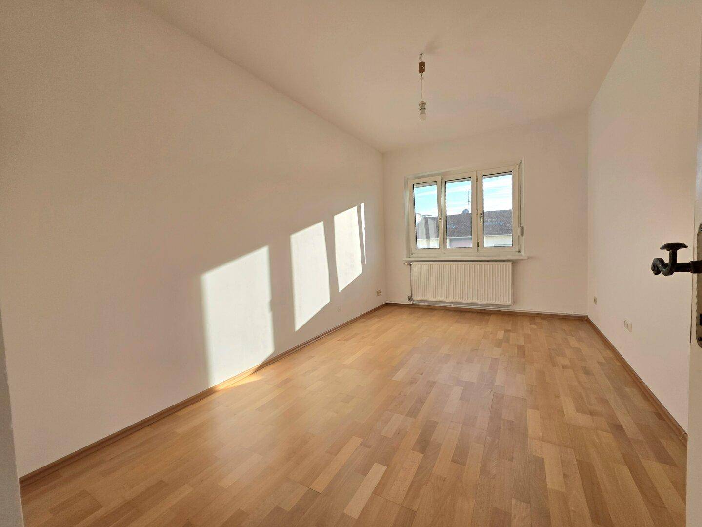 Sonniger Raum mit hellem Parkettboden und weißen Wänden, ideal als Schlaf- oder Arbeitszimmer.