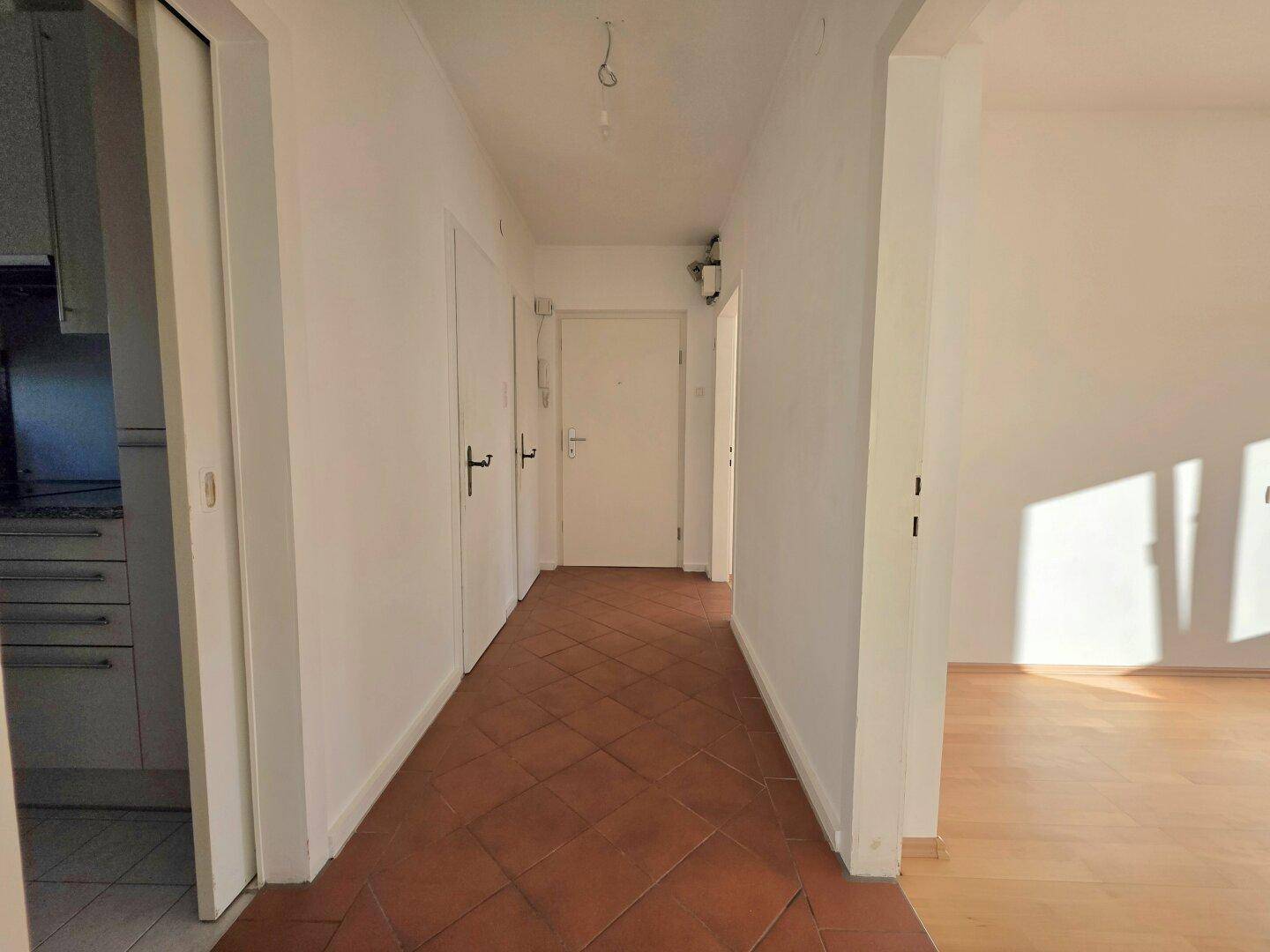 Heller Flur mit Terrakotta-Fliesenboden, weißen Wänden und Zugang zu verschiedenen Räumen.