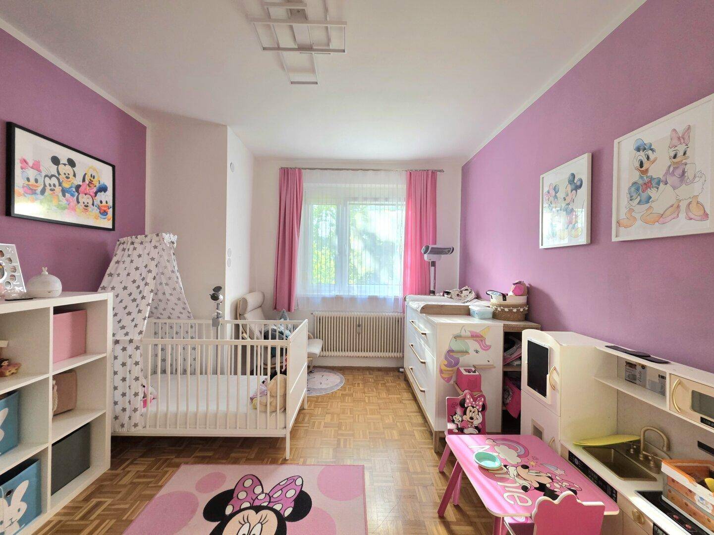 Farbenfrohes Kinderzimmer mit rosa Wänden, Babybett und Spielbereich, ideal für kleine Kinder.