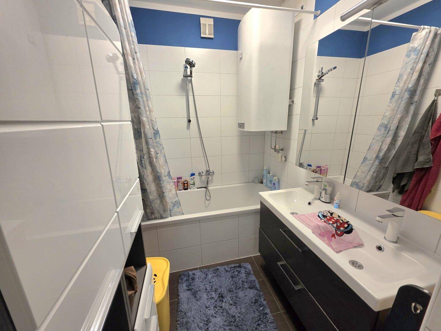 Funktionales Badezimmer mit Badewanne, Duschvorhang und Waschbecken, ausgestattet mit weißen Fliesen.