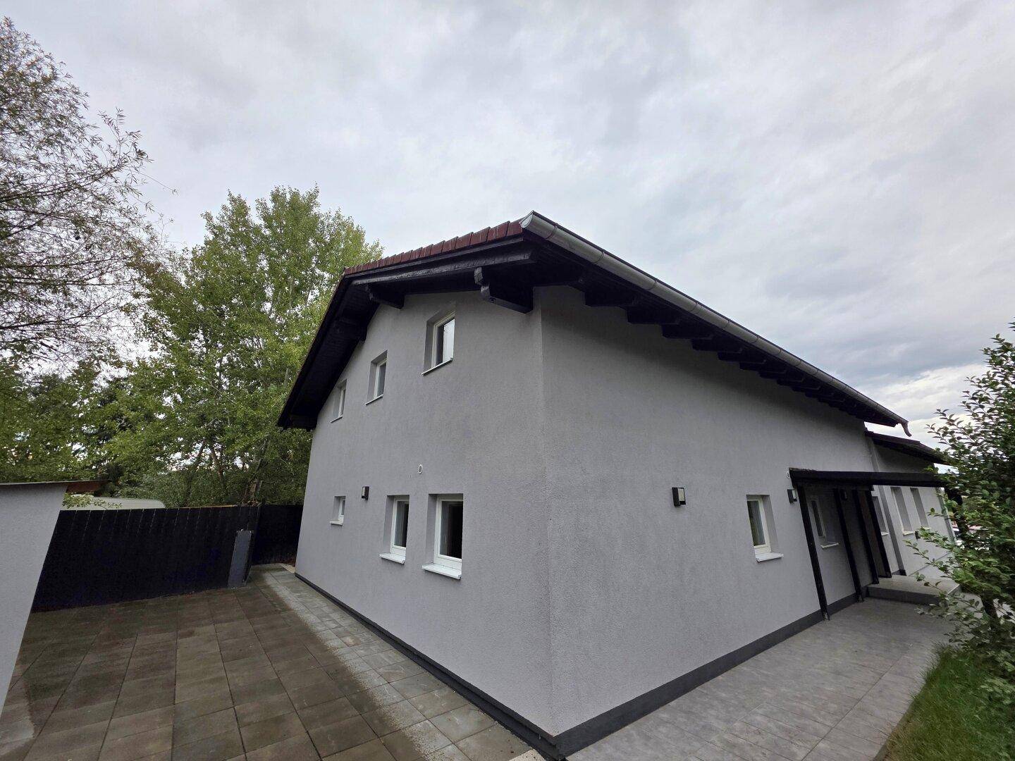 Modernes Einfamilienhaus mit grauer Fassade, Satteldach und gepflastertem Vorplatz.