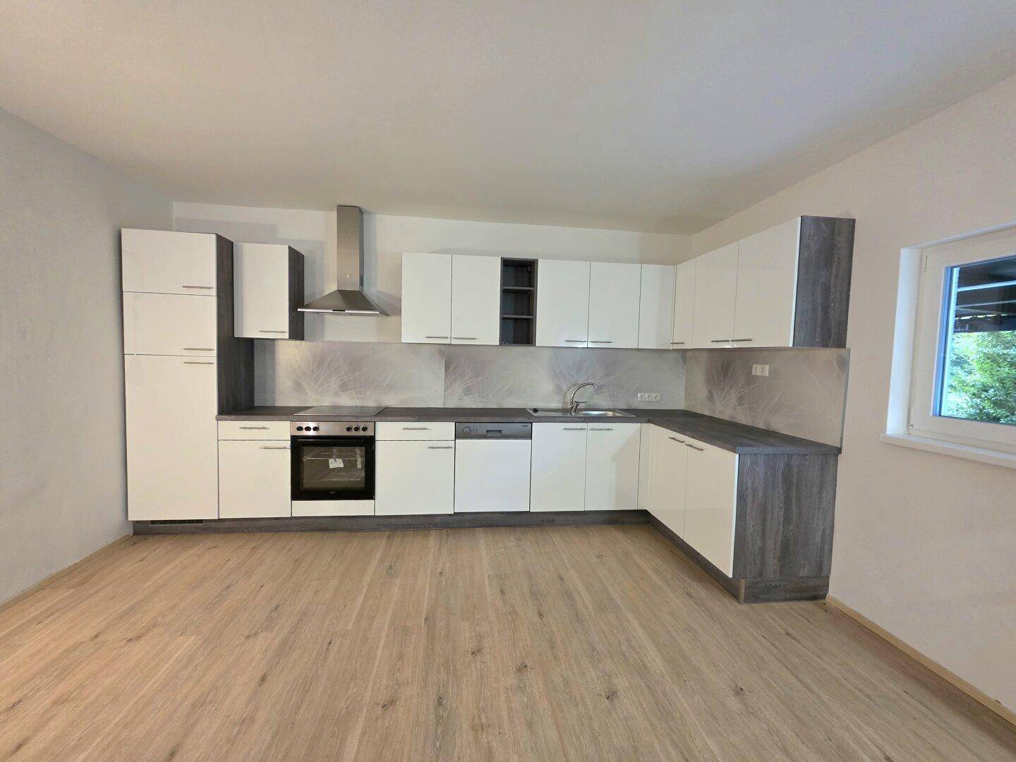 Voll ausgestattete, moderne Küche mit weißen und grauen Schränken, Dunstabzugshaube und Laminatboden.