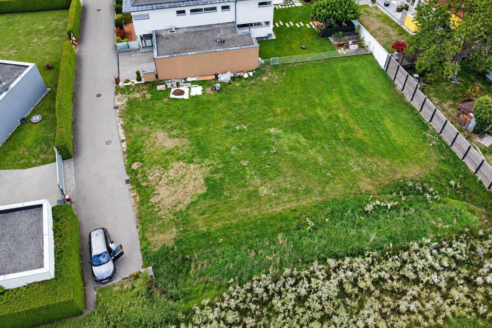 Luftaufnahme eines unbebauten Grundstücks mit angrenzenden Wohnhäusern und einer Zufahrtsstraße.