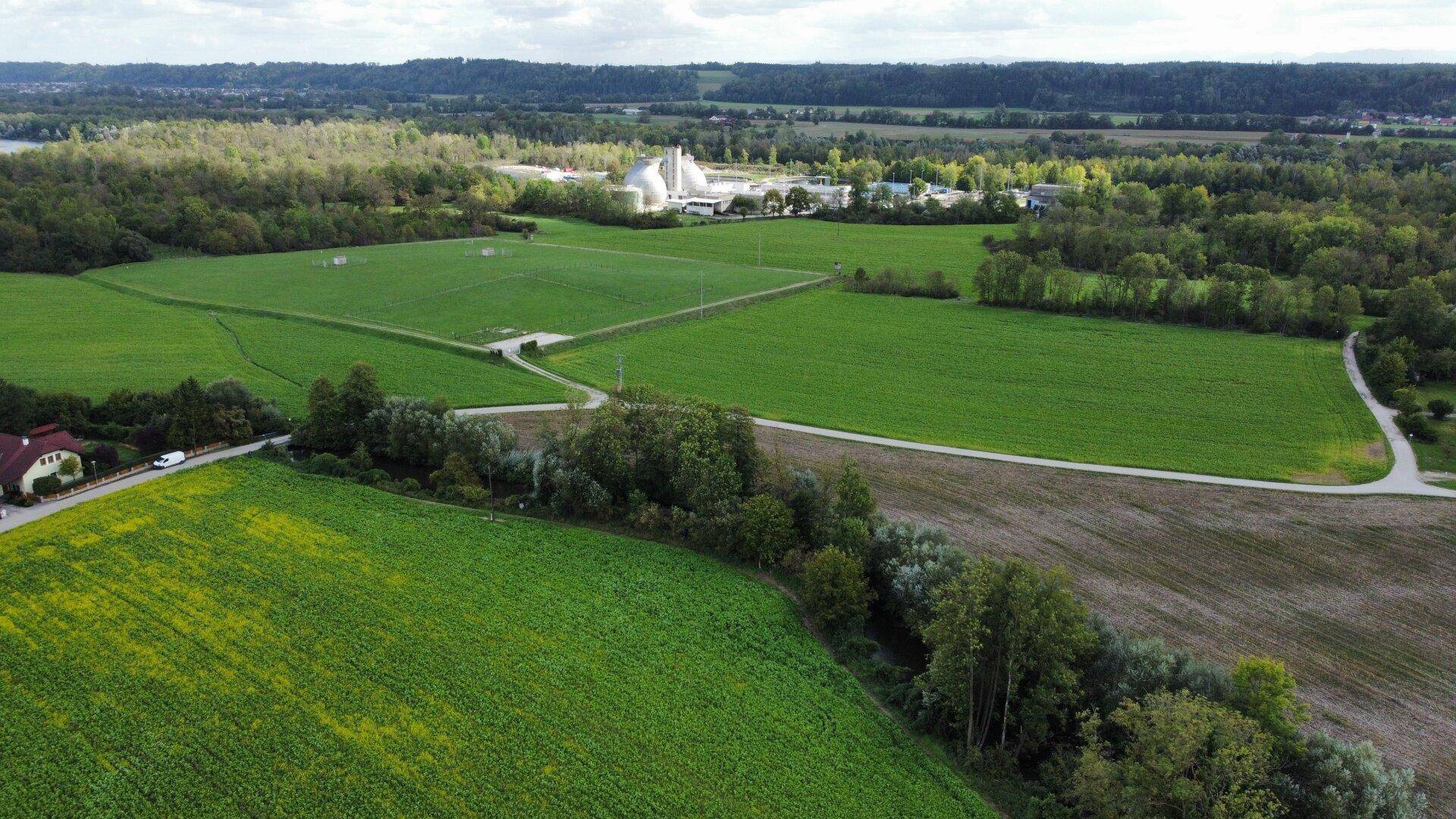 Weitläufige Luftaufnahme einer ländlichen Landschaft mit Feldern, Wäldern und einer Industrieanlage in der Ferne.