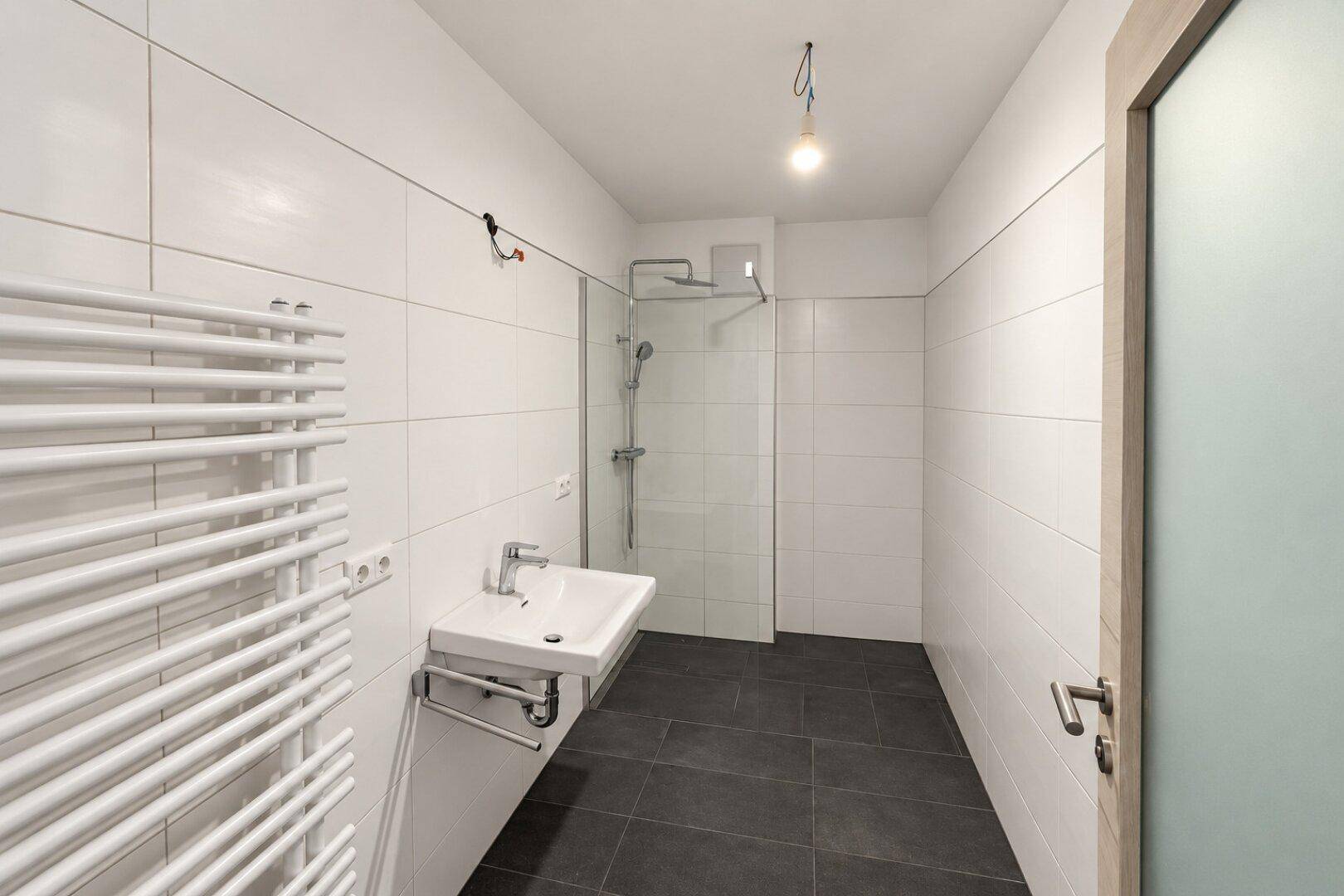 Modernes Badezimmer mit Dusche, weißen Fliesen und beheiztem Handtuchhalter.
