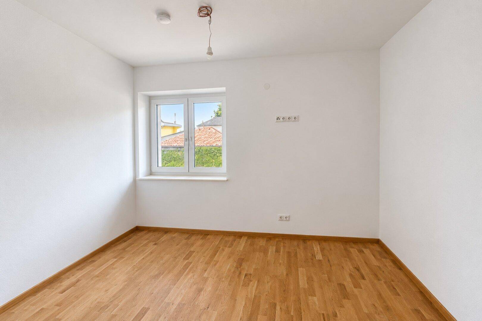 Helles Schlafzimmer mit Parkettboden und Fenster mit Blick ins Grüne.