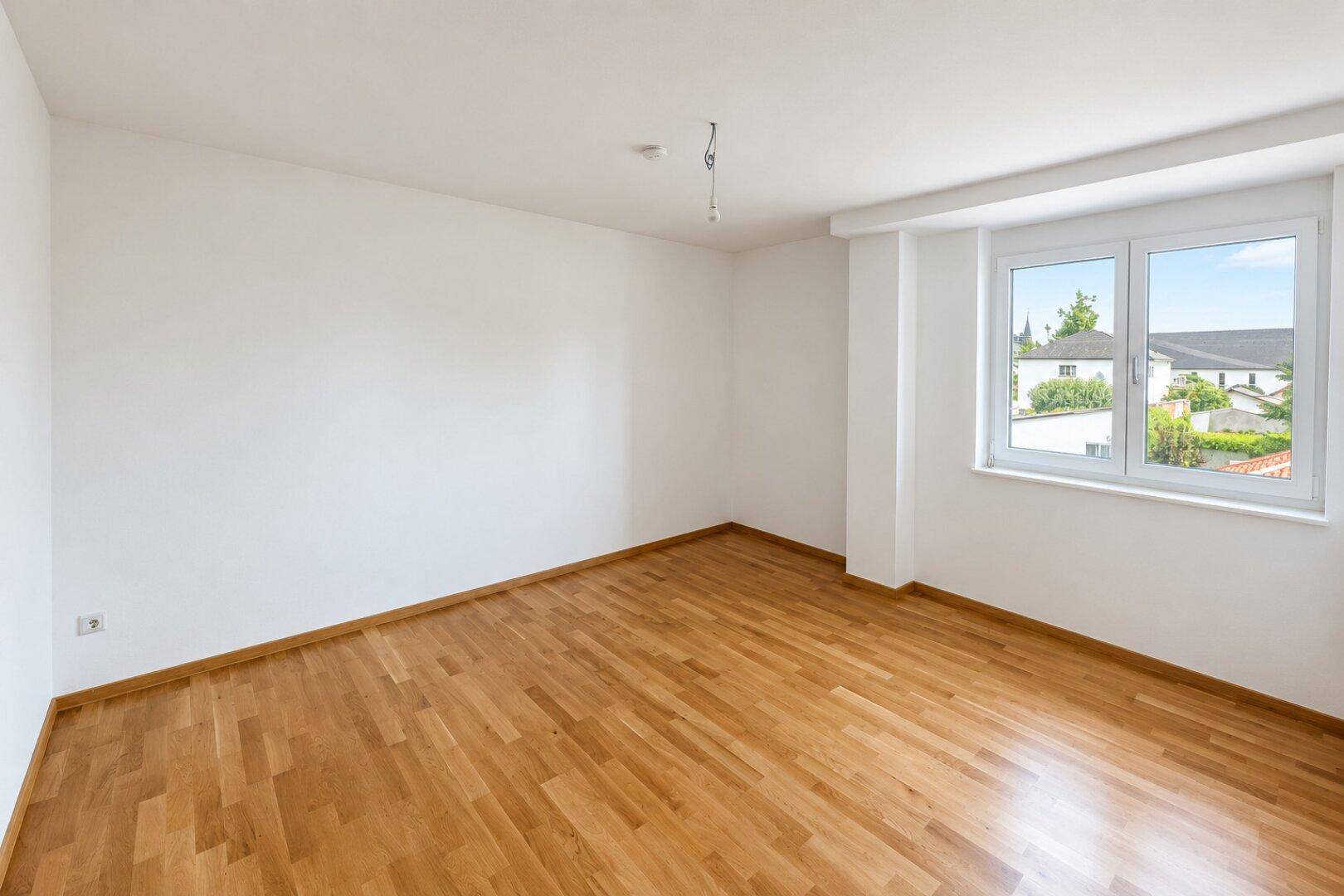 Geräumiges Schlafzimmer mit Parkettboden und großem Fenster für viel Tageslicht.