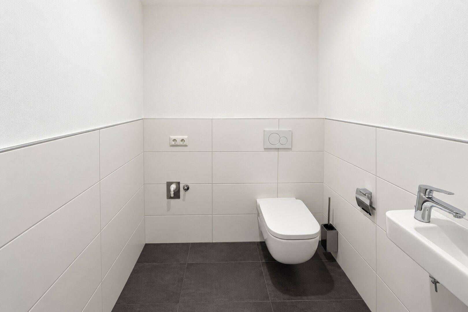 Separates Gäste-WC mit wandhängender Toilette, Waschbecken und dunklen Bodenfliesen.