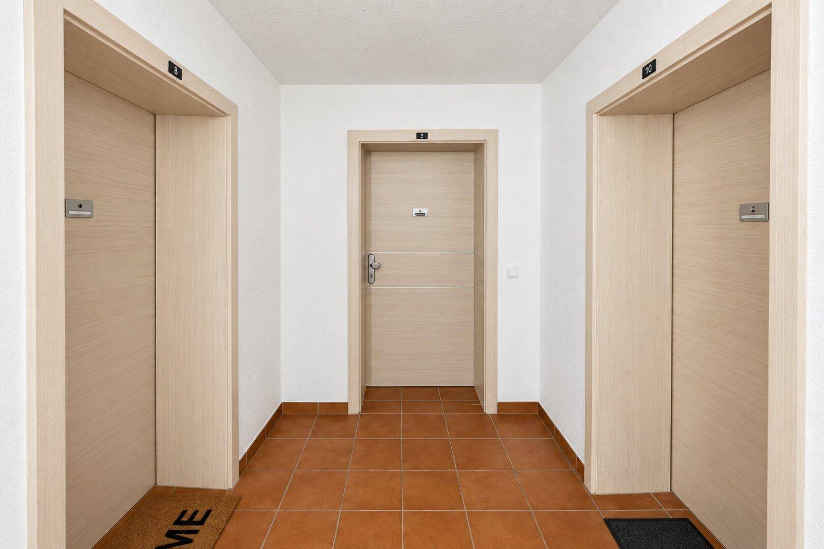 Gemeinschaftlicher Flur mit Terrakotta-Fliesen und mehreren Wohnungseingängen.