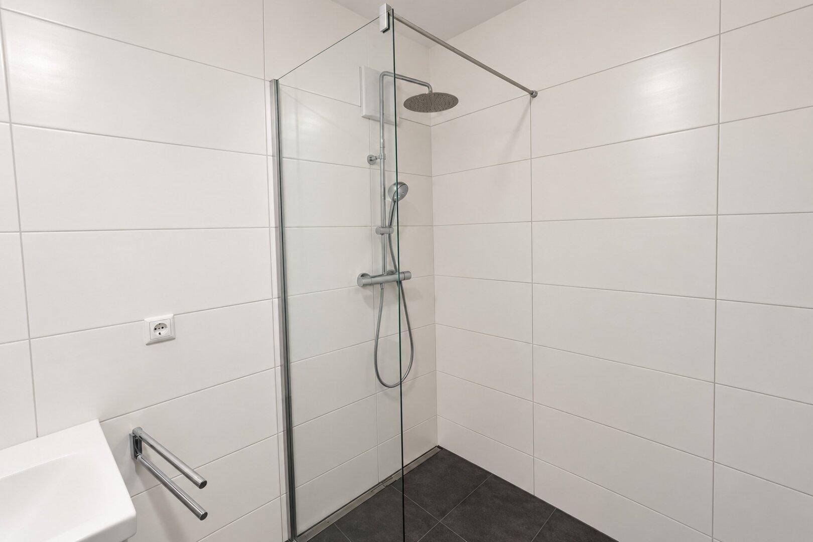 Modernes Badezimmer mit ebenerdiger Dusche, Glasabtrennung und Regenduschkopf, komplett gefliest.