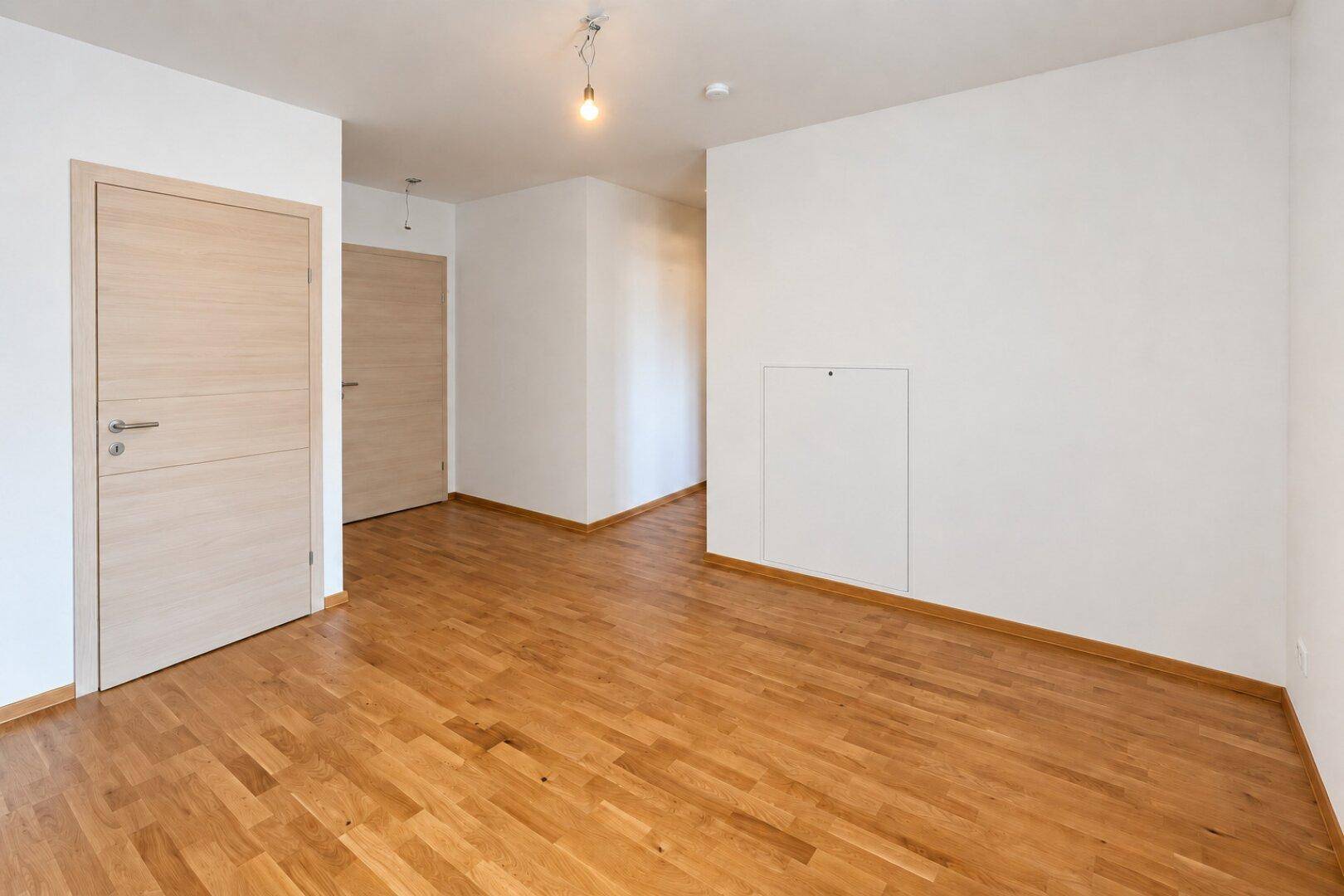 Leeres Zimmer mit hellem Parkettboden und weißen Wänden, bereit zur individuellen Einrichtung und Nutzung.