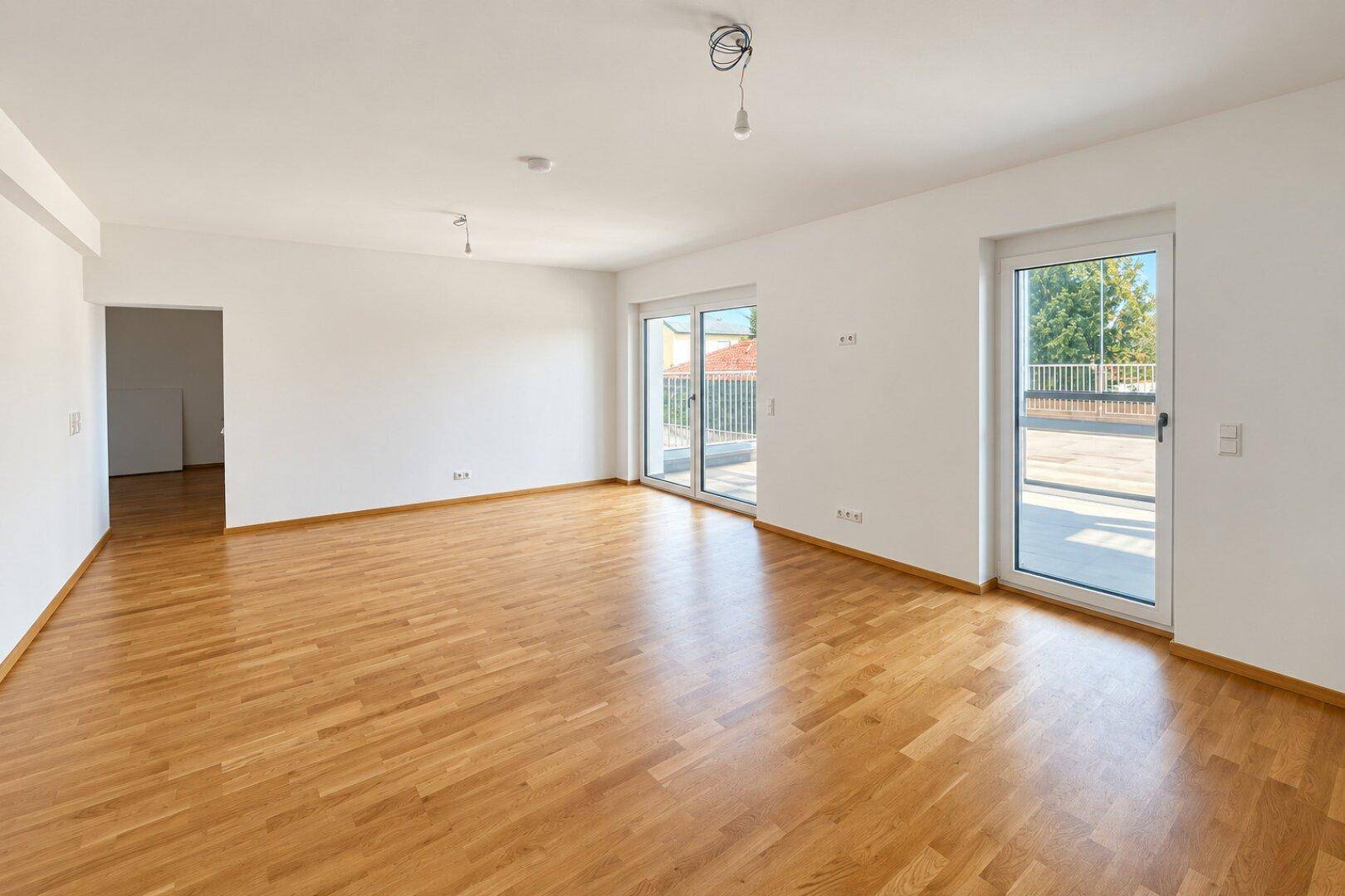 Geräumiges, helles Wohnzimmer mit Parkettboden und Zugang zu einer großen Terrasse durch Schiebetüren.