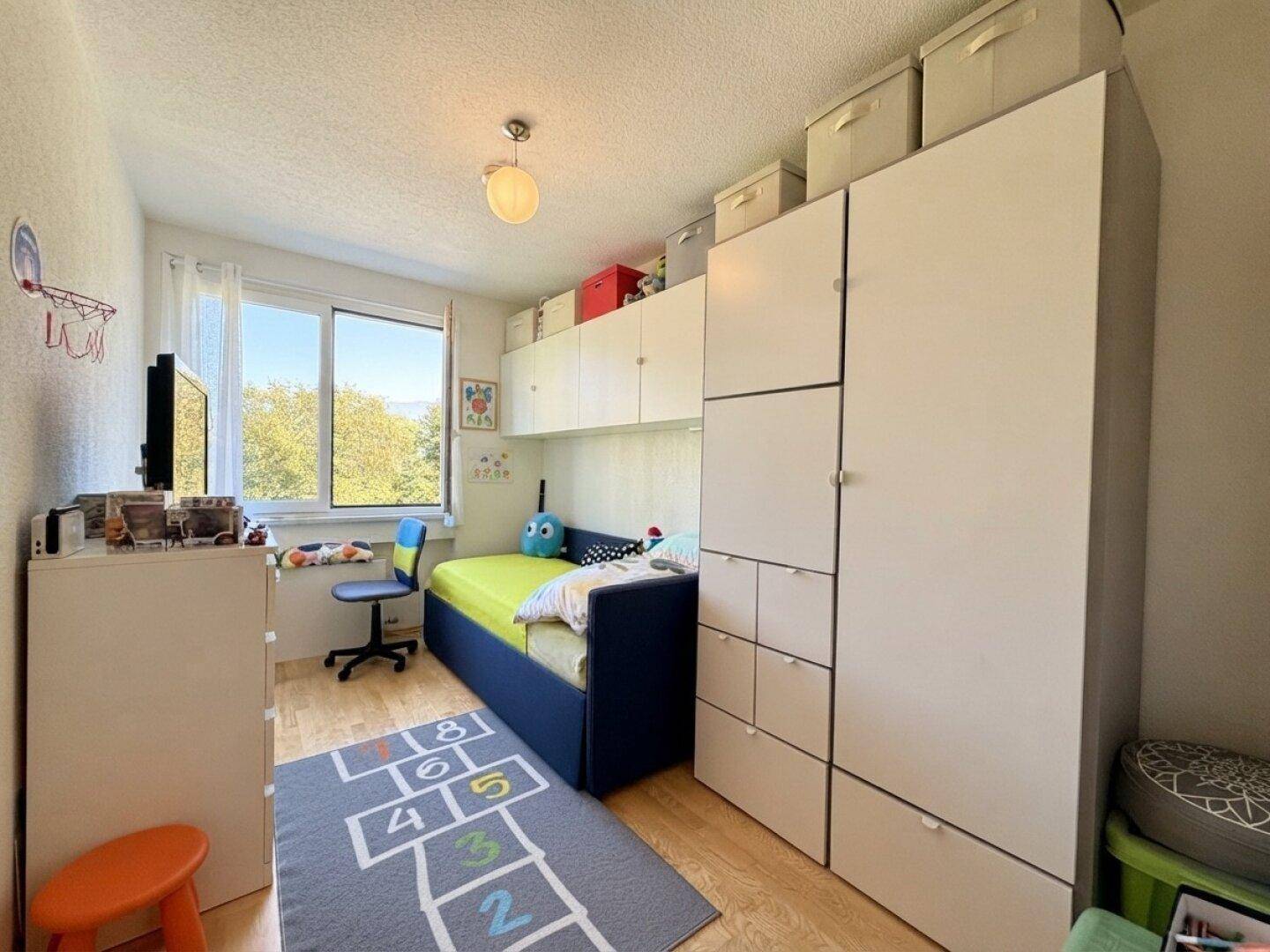 Kinderzimmer mit Bett, Schreibtisch und praktischen Einbauschränken.