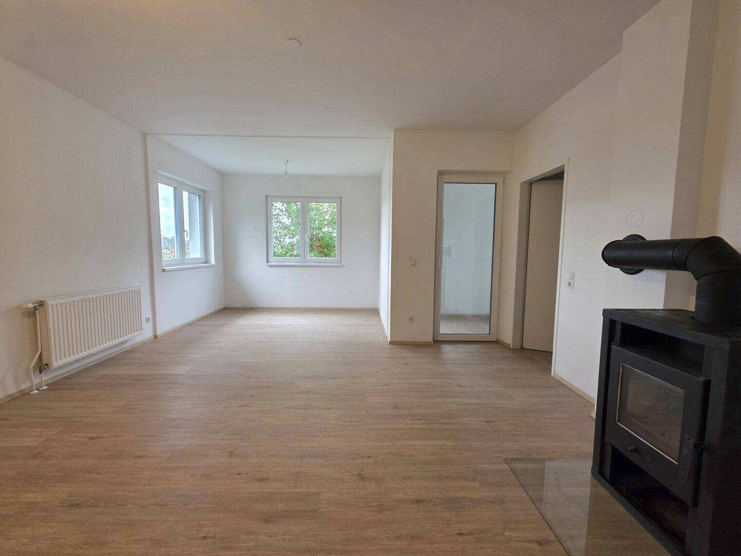 Helles Wohnzimmer mit Laminatboden, großen Fenstern und modernem Holzofen für gemütliche Abende.