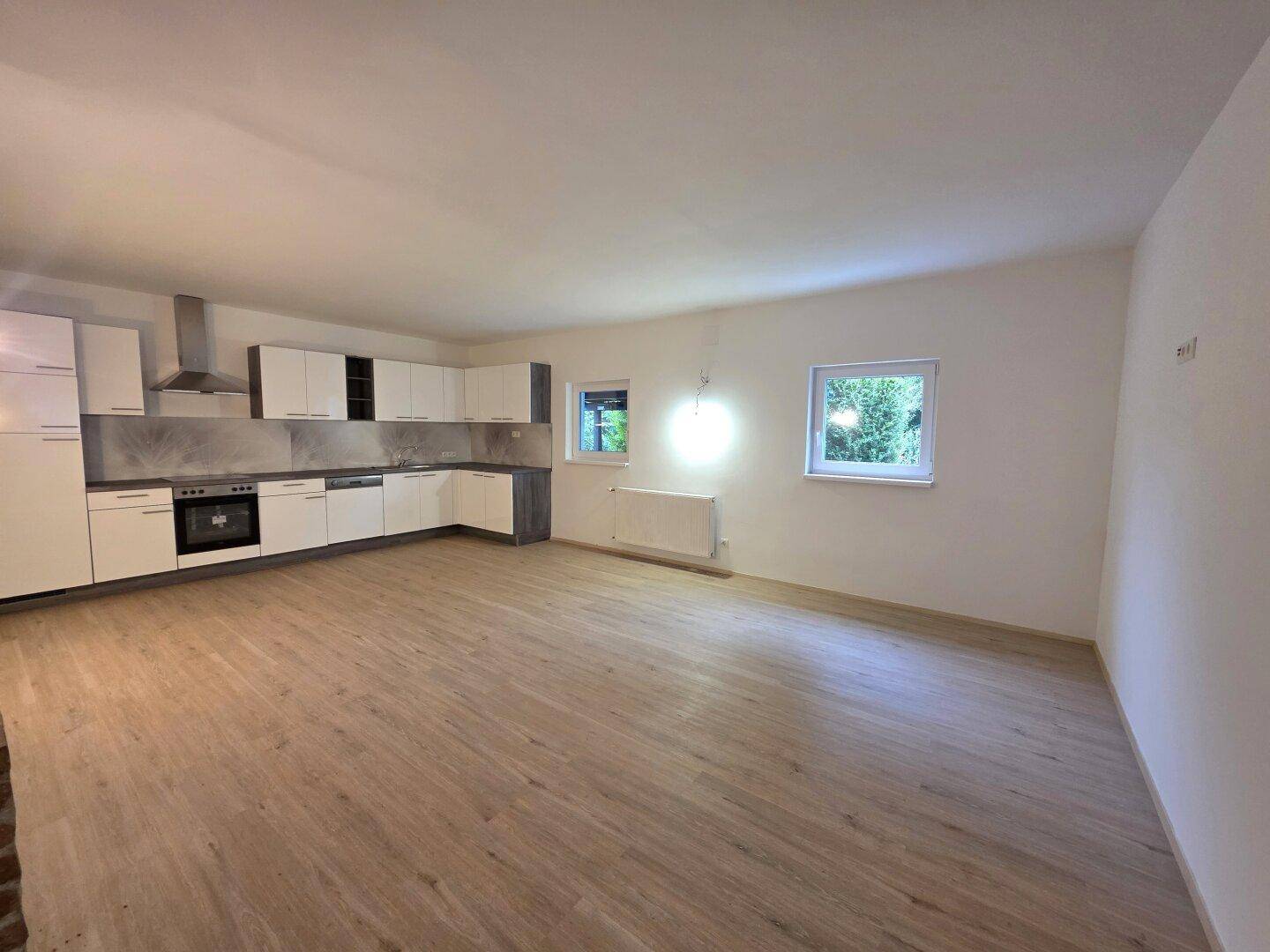 Offener Wohn- und Essbereich mit moderner Einbauküche, Laminatboden und viel Tageslicht.