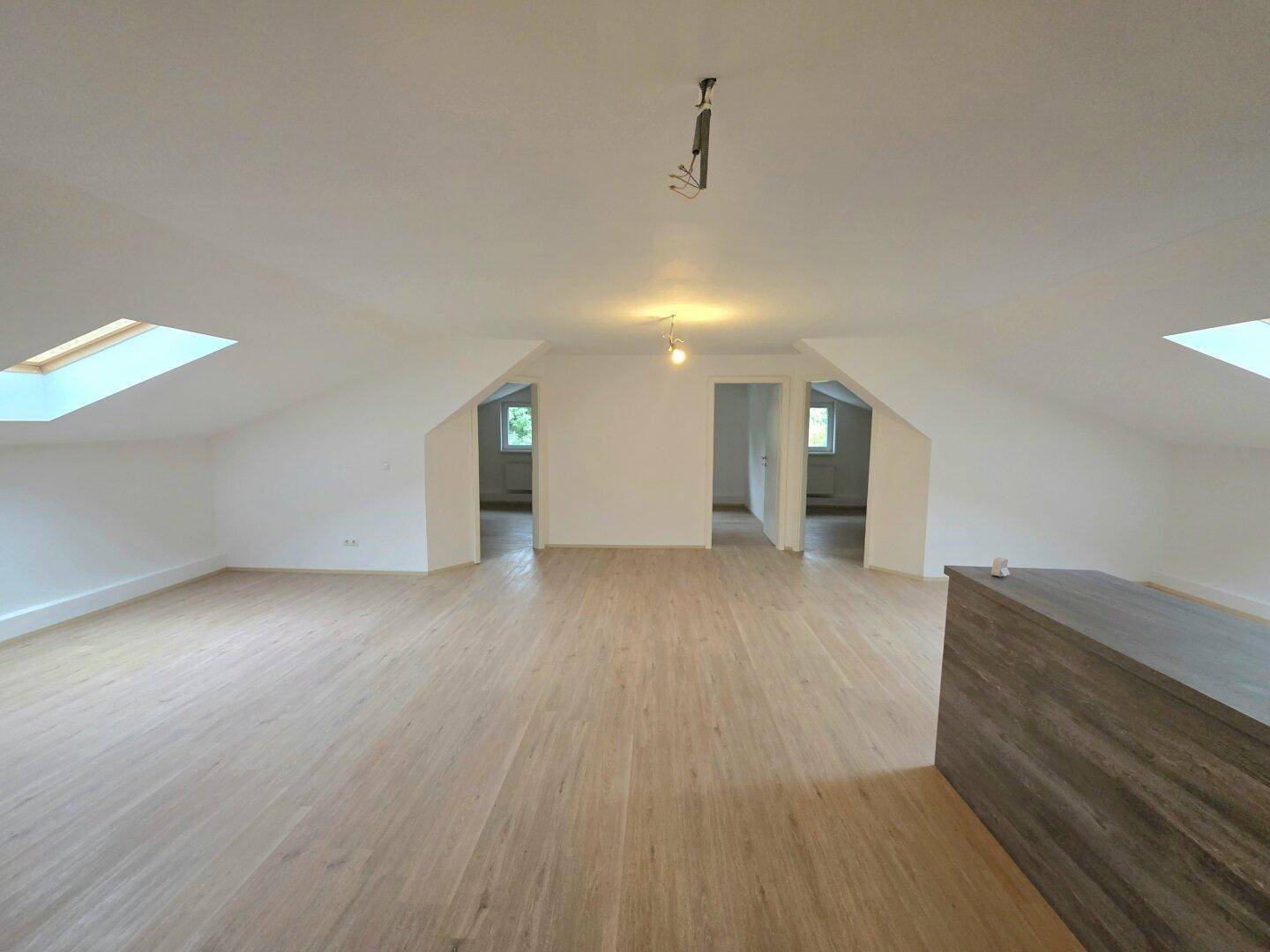Geräumiger offener Raum im Dachgeschoss mit Schrägdach, mehreren Dachfenstern und Laminatboden.