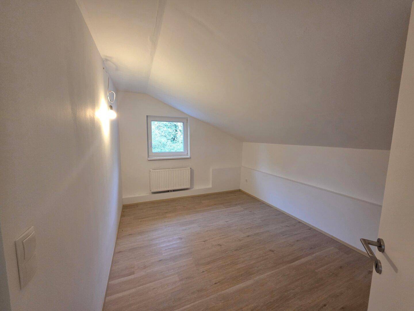Schlafzimmer im Dachgeschoss mit Schrägdach, Laminatboden und Fenster für natürliches Licht.