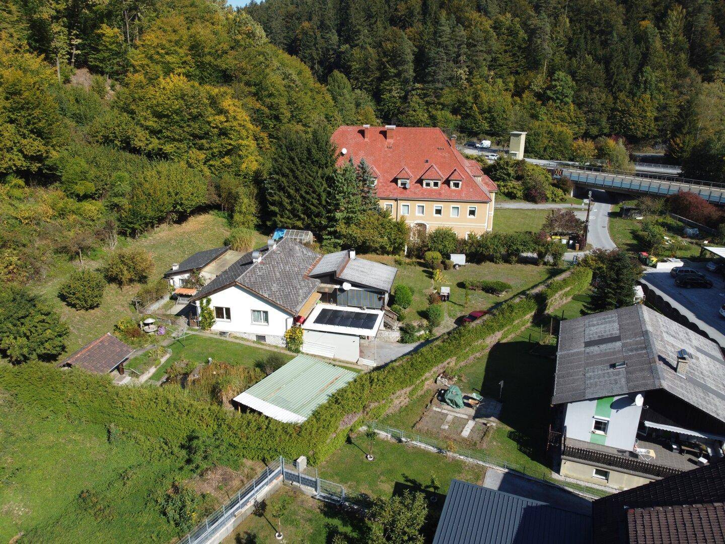 Weitläufige Luftaufnahme des Anwesens mit umliegenden Häusern, Wald und einer Brücke im Hintergrund.