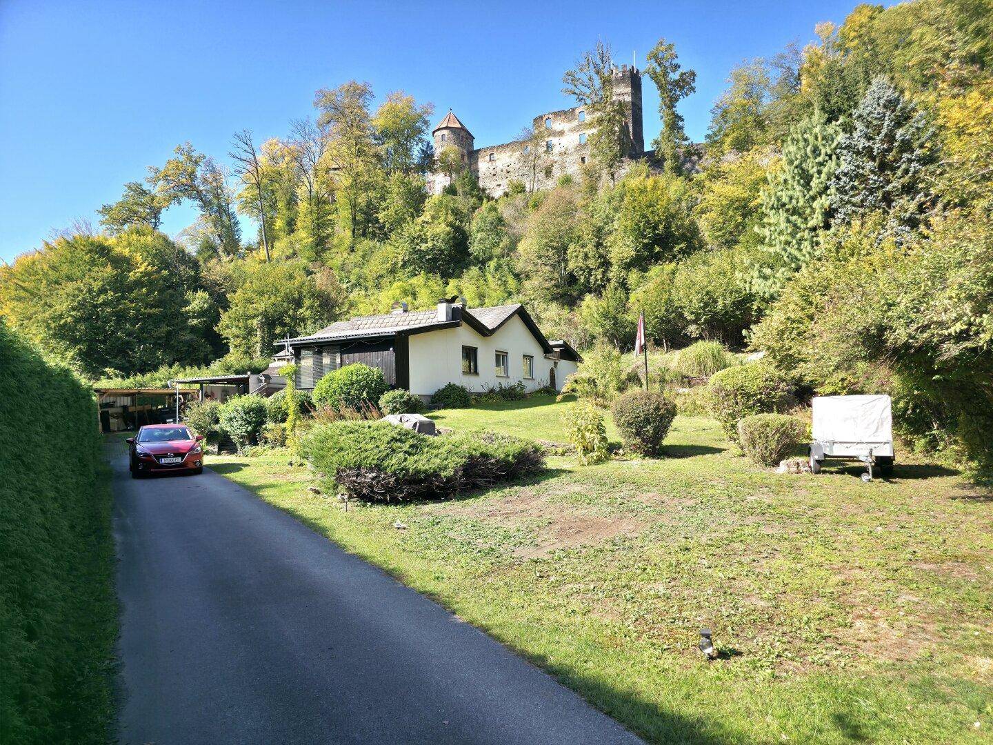 Ansicht des Hauses mit gepflegtem Garten, Auffahrt und der historischen Burg auf dem Hügel im Hintergrund.