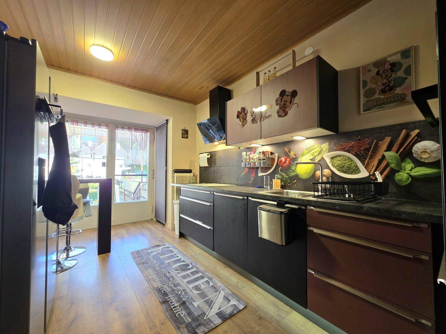Funktionale Küche mit dunklen Schränken, Holzdecke und farbenfroher Rückwand, mit Zugang nach draußen.