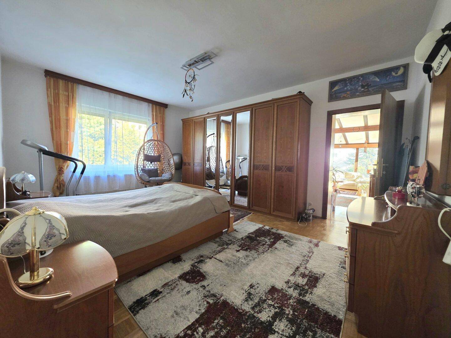 Geräumiges Schlafzimmer mit großem Holzschrank, Bett und Zugang zu einem weiteren Raum.