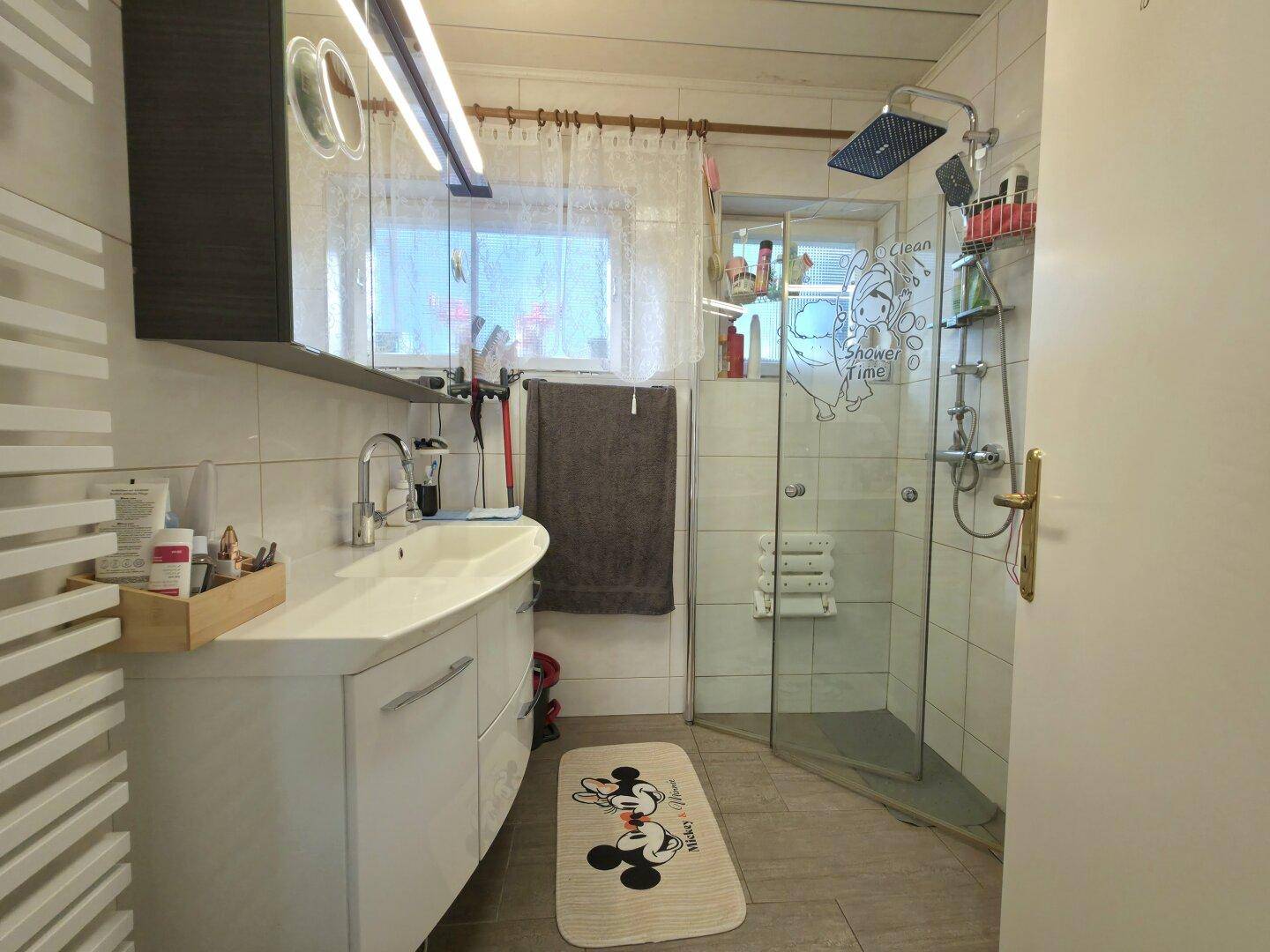 Modernes Badezimmer mit Waschtisch, ebenerdiger Dusche und Regendusche, sowie einem Fenster.